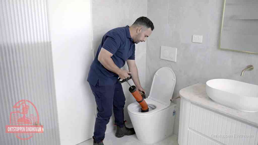 Een monteur buigt over een wandcloset en duwt met de hand een persluchtontstopper in de toiletpot om de verstopping handmatig los te maken in Eindhoven Een monteur buigt over een wandcloset en duwt met de hand een persluchtontstopper in de toiletpot om de verstopping handmatig los te maken in Eindhoven