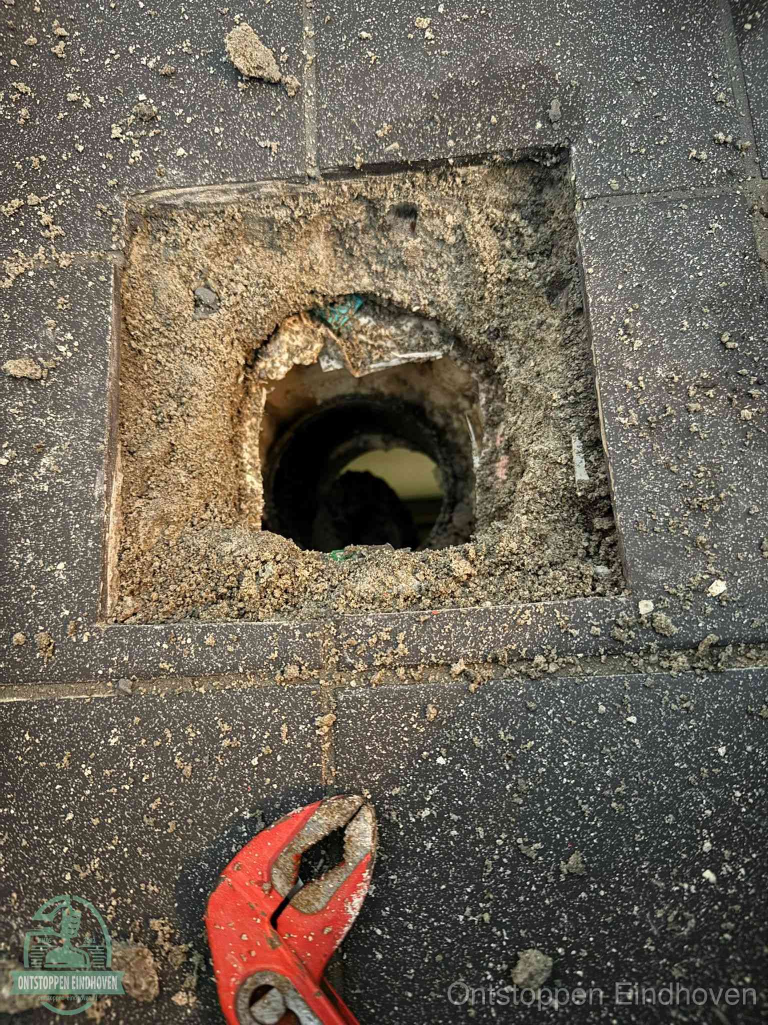 Een geopend rioolputje in een betontegelvloer met losgemaakt rooster en een zichtbare ronde afvoerbuis, het achterhalen waar de afvoerverstopping zit in Eindhoven