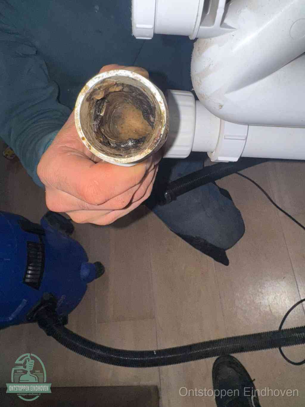Een hand houdt een losgekoppeld PVC-afvoerbuisstuk vast dat van binnen volledig is dichtgeslibd met vet, vuil en aanslag, de meest voorkomende oorzaak van een verstopte afvoer in Eindhoven