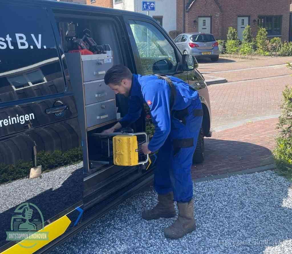 Een monteur pakt buiten op de oprit gereedschap uit de bedrijfsbus, het moment om een professional in te schakelen voor een verstopte afvoer in Eindhoven