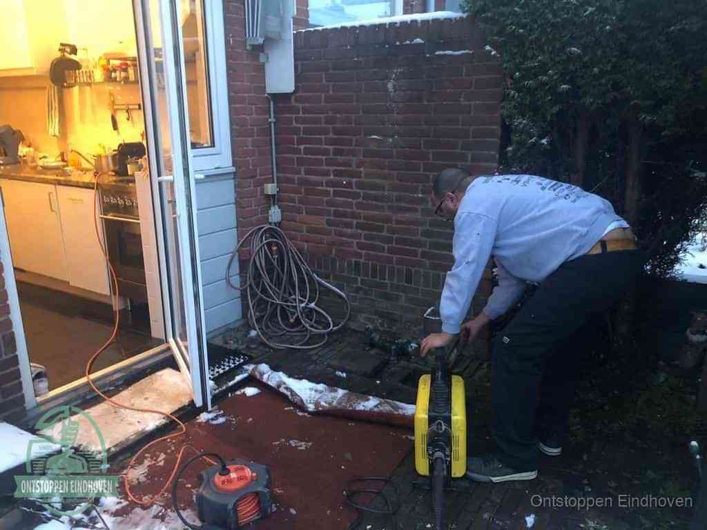 Een monteur werkt buiten bij een open riool-/grondput met een elektrische ontstoppingsmachine om een verborgen afvoerprobleem op te sporen in Eindhoven