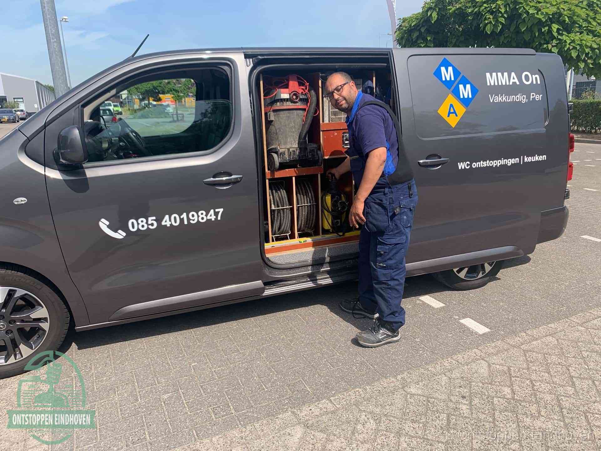Een monteur bij de open schuifdeur van zijn bedrijfsbus op een parkeerplaats, klaar om de oorzaak van terugkerende afvoerverstoppingen aan te pakken in Eindhoven