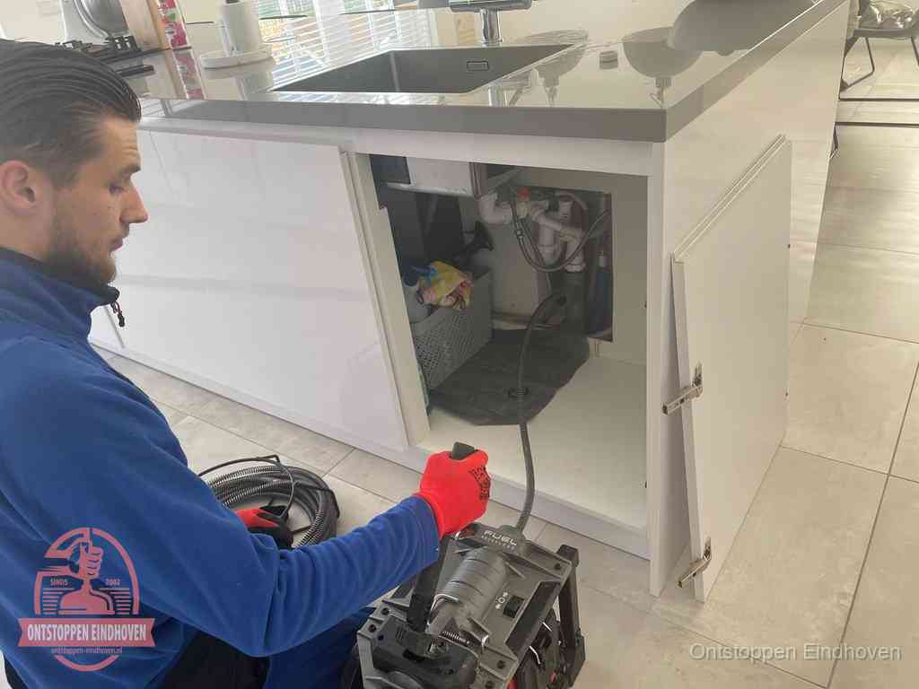 Monteur ontstopt met een veermachine een verstopte afvoer onder de gootsteen in Eindhoven