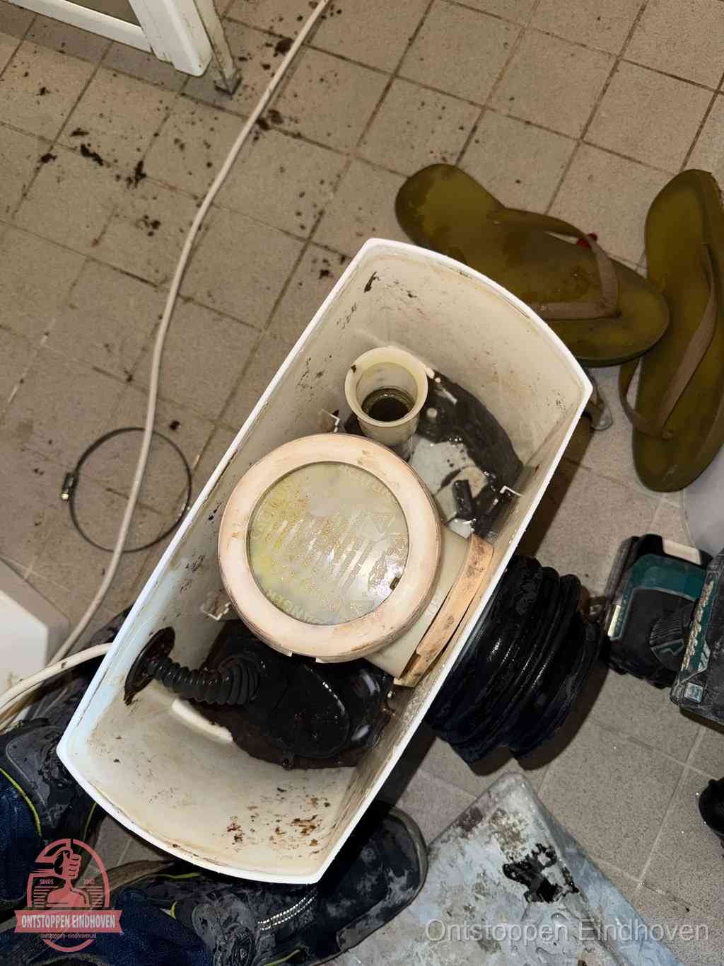 Een gedemonteerde toiletpot op de vloer met ontstoppingsveer en gereedschap ernaast, het verwijderen van een vastzittend voorwerp uit de wc in Eindhoven Een gedemonteerde toiletpot op de vloer met ontstoppingsveer en gereedschap ernaast, het verwijderen van een vastzittend voorwerp uit de wc in Eindhoven