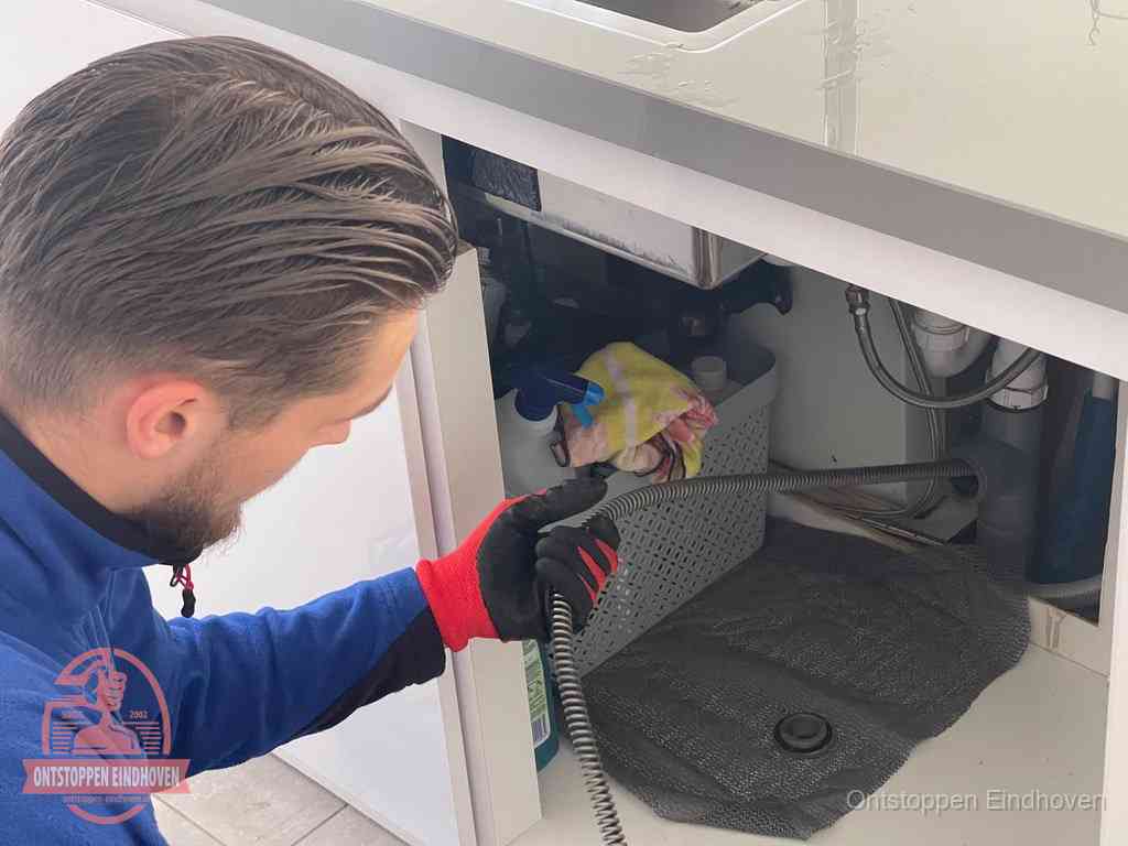 Een monteur voert een flexibele ontstoppingsveer in de afvoer om een verstopping voorbij de bocht van het toilet te bereiken in Eindhoven Een monteur voert een flexibele ontstoppingsveer in de afvoer om een verstopping voorbij de bocht van het toilet te bereiken in Eindhoven