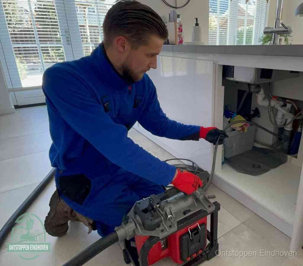 Een monteur met rode handschoenen knielt in een keuken en voert een elektrische ontstoppingsveer in tijdens het professioneel afvoer ontstoppen in Eindhoven
